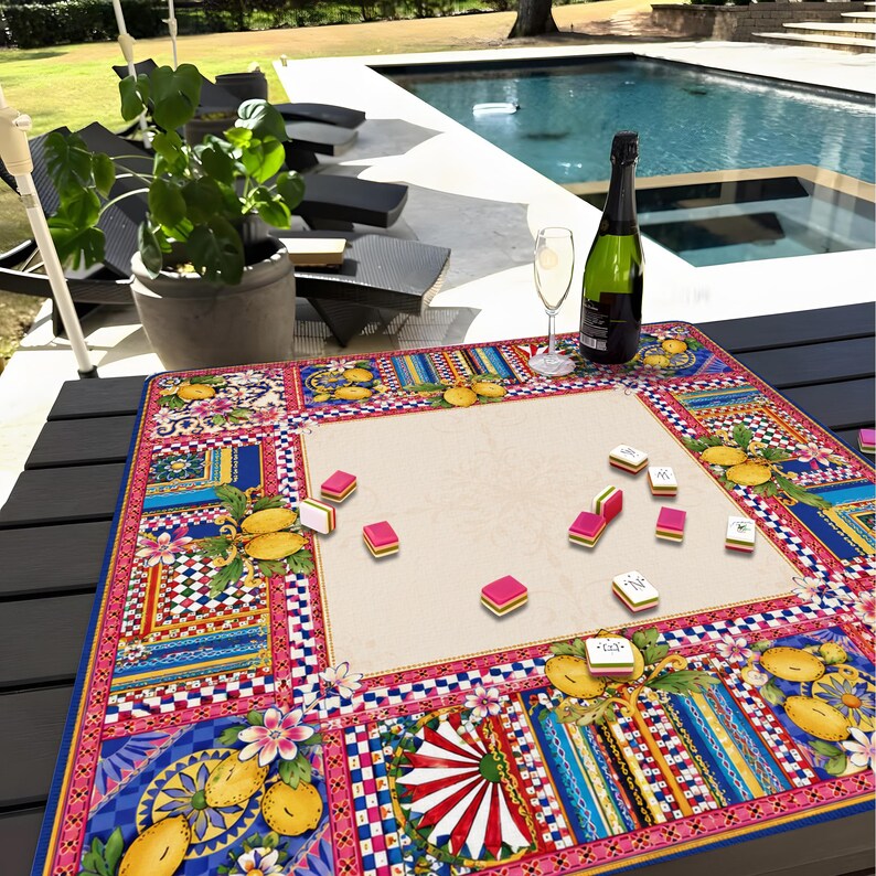 Pode incluir: Um conjunto de jogo de Mahjong colorido numa mesa estampada. A mesa tem um centro creme com uma borda vibrante com desenhos florais e geom&eacute;tricos em rosa, azul e amarelo. Uma garrafa de champanhe e um copo est&atilde;o sobre a mesa.
