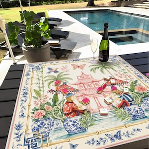 Könnte beinhalten: Eine quadratische Mahjong-Matte mit einem farbenfrohen Chinoiserie-Druck, der Affen, Pagoden, Palmen und florale Motive in Rot-, Blau- und Grüntönen zeigt. Die Matte liegt flach auf einem dunklen Tisch und ist mit verstreuten Mahjong-Spielsteinen bedeckt.