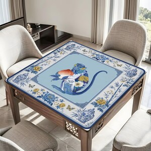 K&ouml;nnte beinhalten: Quadratischer Tisch mit einer blau-wei&szlig; gemusterten Tischdecke mit einer Affenillustration. Der Affe h&auml;lt einen Pfirsich und ist von Blumen- und Schmetterlingsmotiven umgeben. Der Tisch ist aus Holz und hat dekorative Ausschnitte.