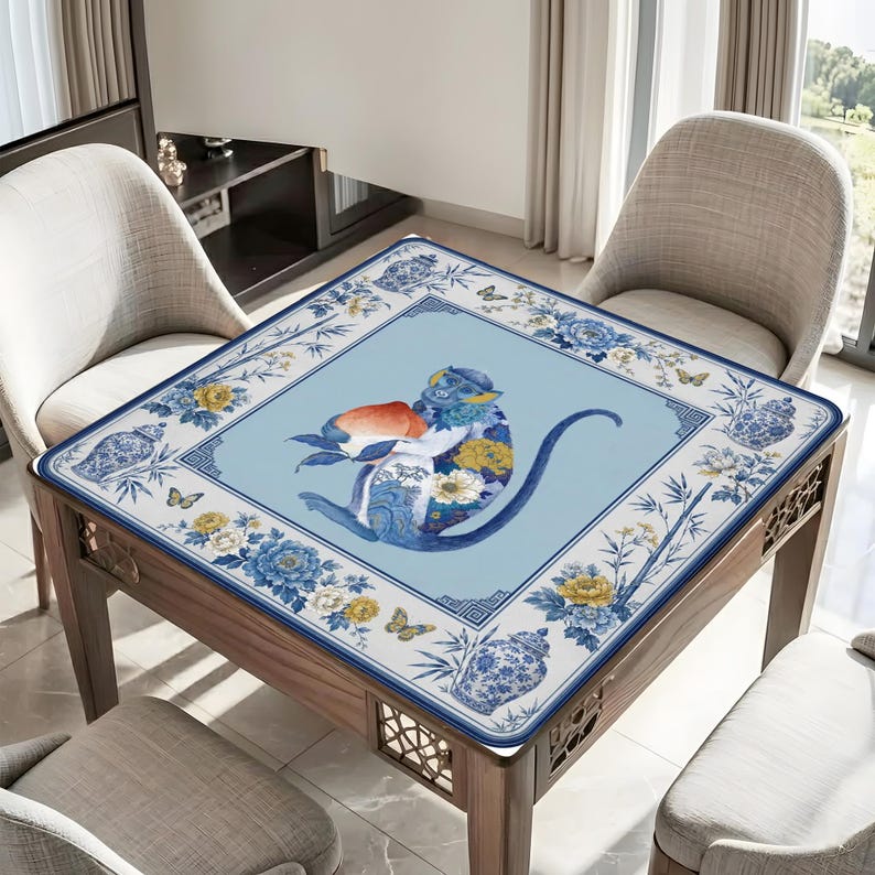 K&ouml;nnte beinhalten: Quadratischer Tisch mit einer blau-wei&szlig; gemusterten Tischdecke mit einer Affenillustration. Der Affe h&auml;lt einen Pfirsich und ist von Blumen- und Schmetterlingsmotiven umgeben. Der Tisch ist aus Holz und hat dekorative Ausschnitte.