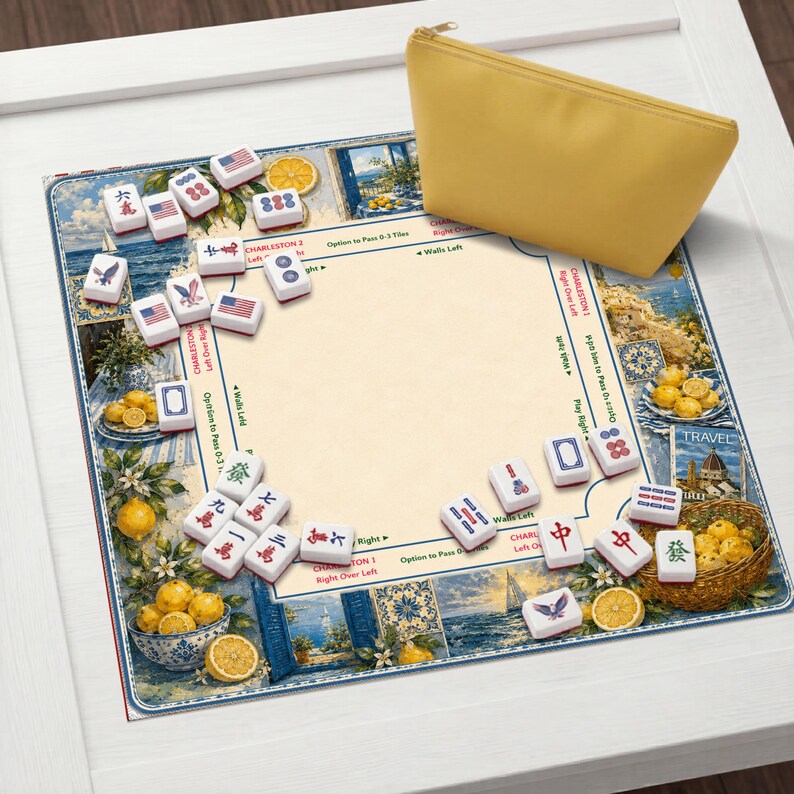 May include: A yellow zippered pouch rests on a game board with a coastal theme. The board features illustrations of lemons, ocean views, and game tiles. The tiles have various symbols and American flag designs. The game board is on a white surface.