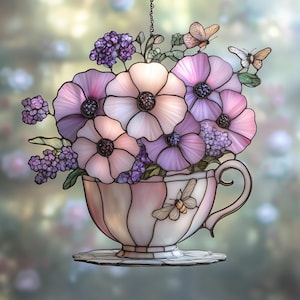 May include: Stained glass floral arrangement in a teacup. The teacup is pink and white with a bee design. The flowers are pink and purple with black centers. Butterflies are perched on the flowers. The teacup sits on a matching saucer.