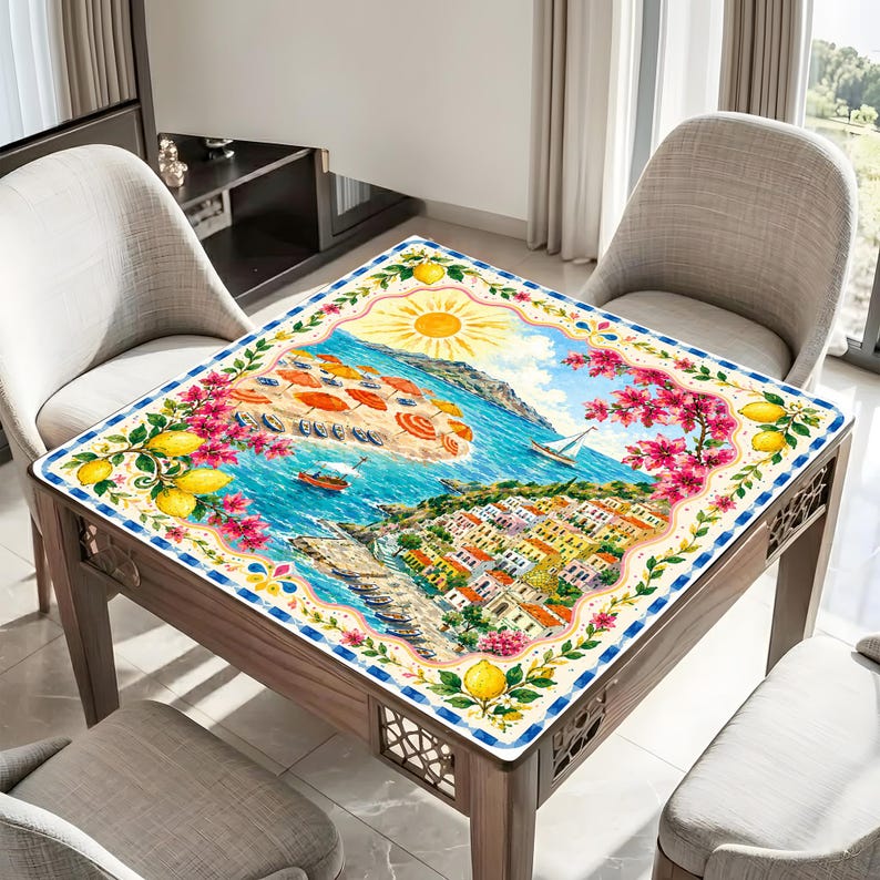 Może przedstawiać: Kwadratowy drewniany st&oacute;ł z kolorową, szczeg&oacute;łową ilustracją sceny nadmorskiej. Grafika przedstawia plażę z parasolami, łodziami i miastem z czerwonymi dachami. St&oacute;ł otoczony jest dwoma krzesłami.