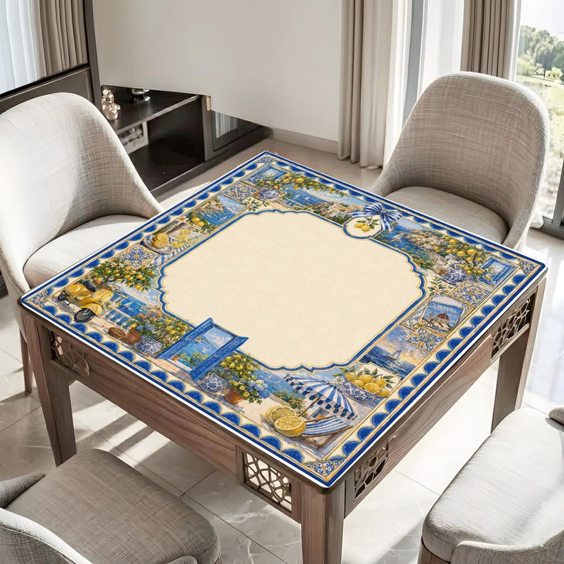 May include: A square wooden table with a decorative, colorful tablecloth featuring a coastal Italian design. The tablecloth has a cream-colored center with a blue border and illustrations of lemons, umbrellas, and seaside scenes. The table is surrounded by three chairs.