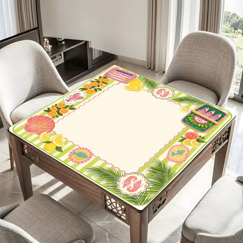 May include: A square wooden table with a decorative mat featuring a cream-colored center and a green and white striped border. The border is adorned with illustrations of seafood, citrus fruits, and palm fronds. The table is surrounded by two chairs.