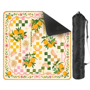 May include: A picnic blanket with a cream background featuring a pattern of oranges, flowers, and checkered squares. The blanket has a black underside and comes with a black carrying bag. The design includes pink, yellow, and green accents.