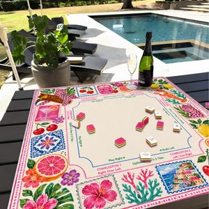 May include: A square mahjong mat featuring a cream-colored center with game instructions and a vibrant border decorated with pink leopards, red cherries, citrus slices, hibiscus flowers, coral, and a coastal village scene, with scattered tiles.