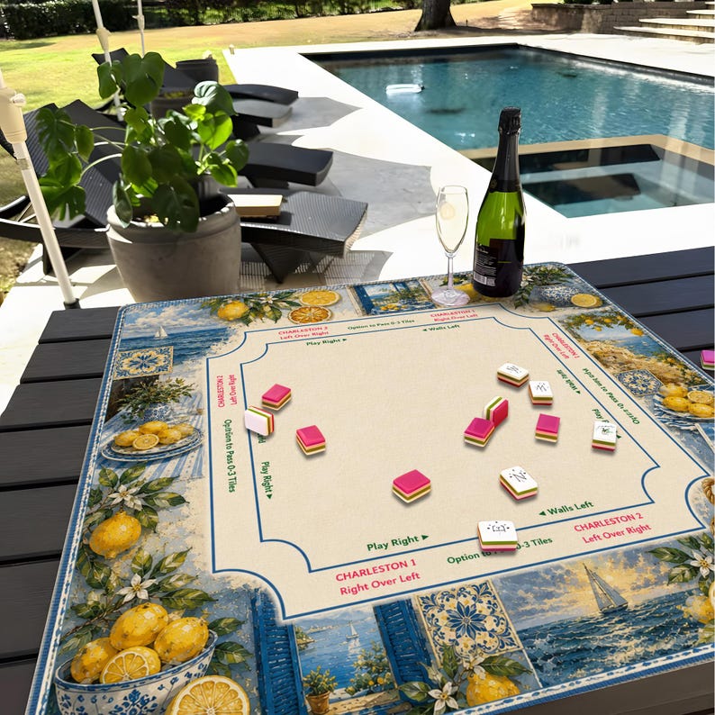May include: A Mahjong game board with a nautical and lemon theme. The board features a cream-colored playing surface with pink and white tiles. A bottle of champagne and a glass are on the table. The board is surrounded by a blue and white border.