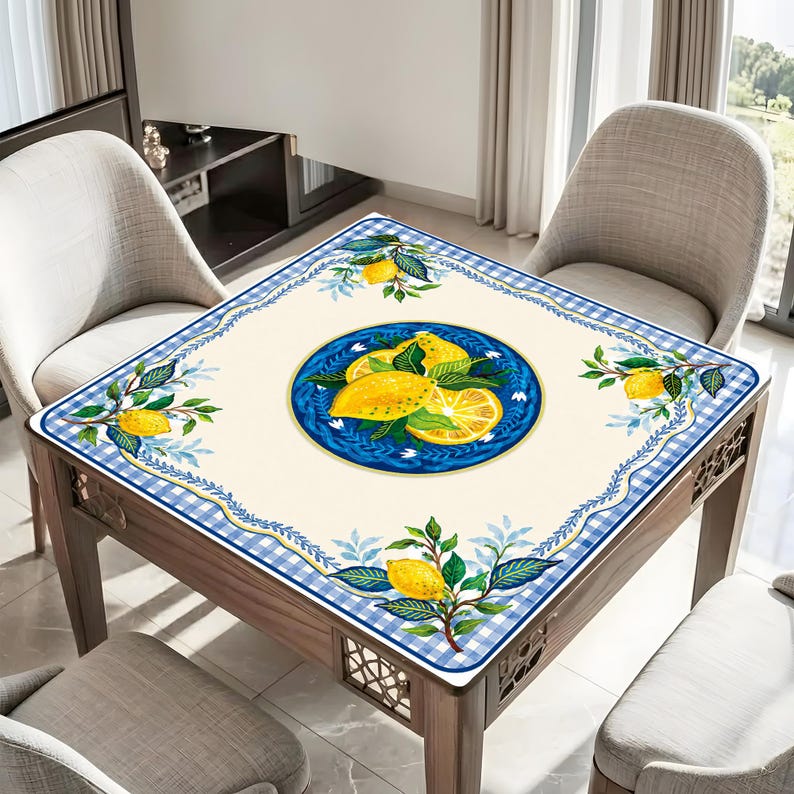 May include: Square table with a cream-colored tablecloth featuring a blue and white checkered border. The tablecloth has a central blue circle with a lemon illustration. Lemon and leaf motifs are also in the corners.