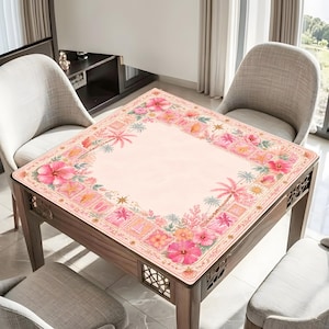 May include: A square table cover featuring a light pink center and a decorative border printed with pink hibiscus flowers, palm trees, seashells, starfish, and coral motifs. The fabric is draped over a square wooden table with lattice side panels.