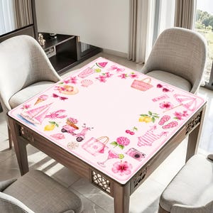 Puede incluir: Un mantel cuadrado con fondo rosa claro y un borde de ilustraciones en acuarela que incluyen un velero, un scooter, un traje de ba&ntilde;o, una bolsa de playa, gafas de sol, flores tropicales, frutas y varios accesorios de tem&aacute;tica veraniega.