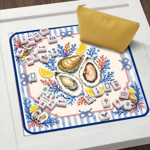 May include: A decorative mahjong set with tiles featuring American flag designs, oysters, and lemon slices. The set includes a yellow zippered pouch and is set on a blue and white striped mat.