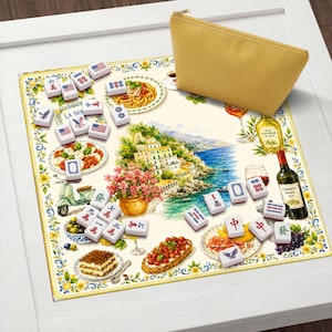 May include: A square play mat featuring a colorful Italian coastal scene with illustrations of food, a scooter, and wine, scattered with white mahjong tiles marked with red, blue, and black symbols and American flags, accompanied by a yellow zippered pouch.
