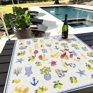 Puede incluir: Un mantel cuadrado de color crema con un borde azul y un patr&oacute;n repetido de limones, anclas y c&oacute;cteles. Una botella de champ&aacute;n y una copa est&aacute;n sobre la mesa. Varios caramelos peque&ntilde;os y coloridos est&aacute;n esparcidos sobre el mantel.