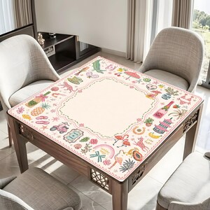 Pu&ograve; includere: Una tovaglia quadrata con un centro color crema e un bordo decorativo con illustrazioni colorate di fenicotteri, ananas, scooter, bottiglie di champagne, palme e vari motivi tropicali stampati in rosa, verde e giallo.