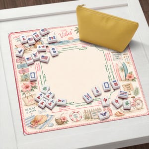 May include: A mahjong game set featuring a rectangular play mat with a beach-themed illustration, including surfboards, a bicycle, and tropical flowers. The mat includes game instructions and text like Good Vibes. Includes white tiles and a yellow pouch.