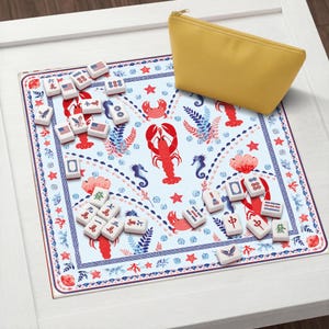 K&ouml;nnte beinhalten: Eine quadratische Spielmatte mit hellblauem Hintergrund, verziert mit einem Muster aus roten Hummern, Krabben und Seepferdchen, umrandet von einem blau-roten geometrischen Design. Wei&szlig;e Mahjong-Steine mit Symbolen und US-Flaggen liegen neben einer gelben Tasche.