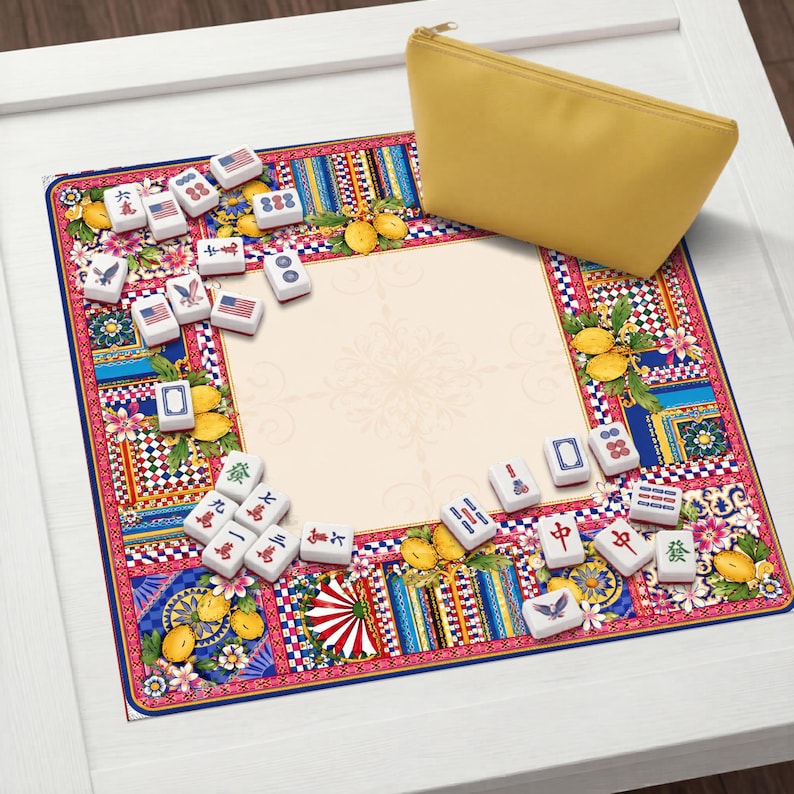 Pode incluir: Um conjunto de jogo de Mahjong colorido com um tapete estampado com desenhos florais e geom&eacute;tricos, lim&otilde;es e pe&ccedil;as com bandeiras americanas. Uma bolsa amarela com z&iacute;per est&aacute; no canto superior direito. As pe&ccedil;as s&atilde;o brancas com s&iacute;mbolos.