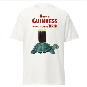 May include: White t-shirt with a graphic of a turtle carrying a glass of Guinness beer. The text on the shirt reads "Have a GUINNESS when you're TIRED."