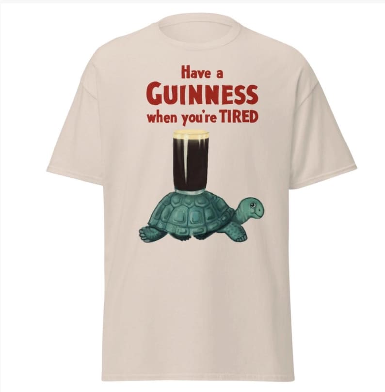 May include: A beige t-shirt with a graphic of a turtle carrying a glass of Guinness beer. The text on the shirt reads "Have a GUINNESS when you're TIRED."