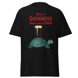 May include: Black t-shirt with a graphic of a turtle carrying a glass of Guinness beer. The text on the shirt reads "Have a Guinness when you're tired."