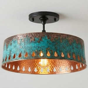 May include: A ceiling-mounted light fixture with a copper-colored interior and a turquoise and copper exterior. The shade has a series of teardrop-shaped cutouts. The fixture is attached to a black base.
