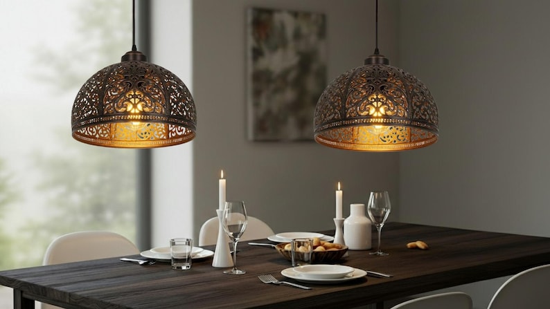 K&ouml;nnte beinhalten: Zwei verzierte Pendelleuchten in Bronze h&auml;ngen &uuml;ber einem Esstisch. Die Lampen haben ein detailliertes, durchbrochenes Design und werfen warmes Licht. Der Tisch ist mit Kerzen, Tellern und Gl&auml;sern gedeckt, was eine einladende Atmosph&auml;re schafft.