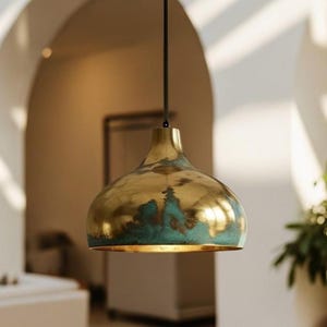 May include: A brass pendant light fixture with a gold finish and turquoise accents. The light hangs from a black cord and has a rounded, bell-shaped shade. The fixture is suspended in a room with arched doorways and natural light.