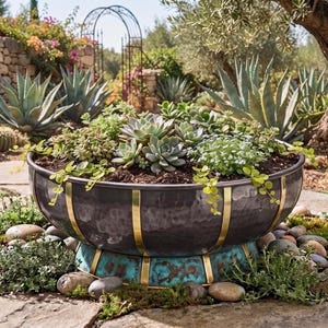 Puede incluir: Una maceta grande y redonda de metal martillado con acabado gris oscuro y tiras verticales color latón. La base presenta un acabado de pátina oxidada en tono turquesa con detalles en latón. La maceta está llena de diversas plantas suculentas.
