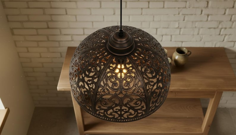 K&ouml;nnte beinhalten: Verzierte, bronzefarbene Pendelleuchte mit kugelf&ouml;rmigem Design. Die Leuchte hat ein kompliziertes, durchbrochenes Muster, das Licht durchscheinen l&auml;sst. Die Leuchte h&auml;ngt an einem schwarzen Kabel und beleuchtet einen Holztisch.