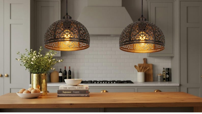 K&ouml;nnte beinhalten: Zwei dekorative Pendelleuchten mit aufwendigen, durchbrochenen Metallschirmen h&auml;ngen &uuml;ber einer K&uuml;cheninsel aus Holz. Die Schirme haben einen warmen, goldenen Innenraum, und die K&uuml;che hat eine neutrale Farbpalette mit einem wei&szlig;en Fliesenspiegel.