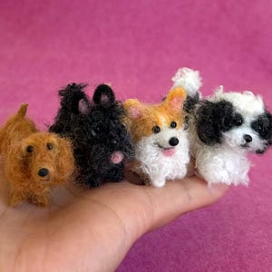 May include: Four miniature needle-felted dog figurines. The first is a solid brown dog, the second is a solid black dog, the third is a tan and white dog with pointed ears, and the fourth is a white dog with black patches around the eyes and ears.