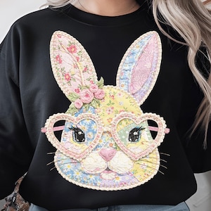 May include: Black sweatshirt featuring a patchwork bunny face with heart-shaped glasses. The bunny has floral patterned ears and face, with pink roses and a pink nose. The glasses are pink and the bunny's eyes are black.