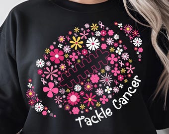 May include: Black sweatshirt with a floral football design. The football is composed of pink, white, and yellow flowers, with pink ribbons. The words "Tackle Cancer" are written in white.