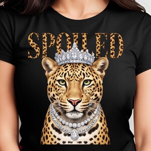 May include: Black t-shirt featuring a leopard illustration wearing a diamond crown and necklace. The word "SPOILED" is printed above the leopard's head in a leopard print font. The leopard has green eyes and a pink nose.