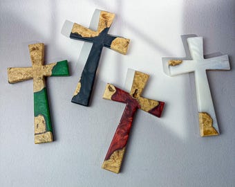 May include: Four wooden crosses with epoxy resin in various colors: green, black, red, and white. The crosses have a natural wood grain pattern and are set against a white background. Each cross is unique, showcasing the natural beauty of the wood and resin.