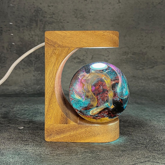A handmade resin globe filled with swirling cosmic smoke and LED galaxy lighting, framed in a moon arch — moody sci-fi desk art that looks like a captured nebula.