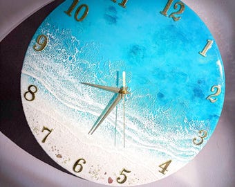 Puede incluir: Reloj de pared redondo con diseño de playa. La esfera del reloj presenta un degradado de azul y blanco, que recuerda a las olas del océano y la arena. Los números dorados marcan las horas, y las manecillas doradas indican la hora. El diámetro del reloj es de unos 30 cm.