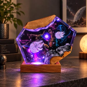 Könnte beinhalten: Eine sechseckige Harz- und Holzlampe mit einer Weltraumszene, in die zwei Millennium Falcon Raumschiffmodelle eingebettet sind. Das klare Harz enthält wirbelnde violette und blaue Nebelmuster und wird von einem Holzsockel mit LED beleuchtet.