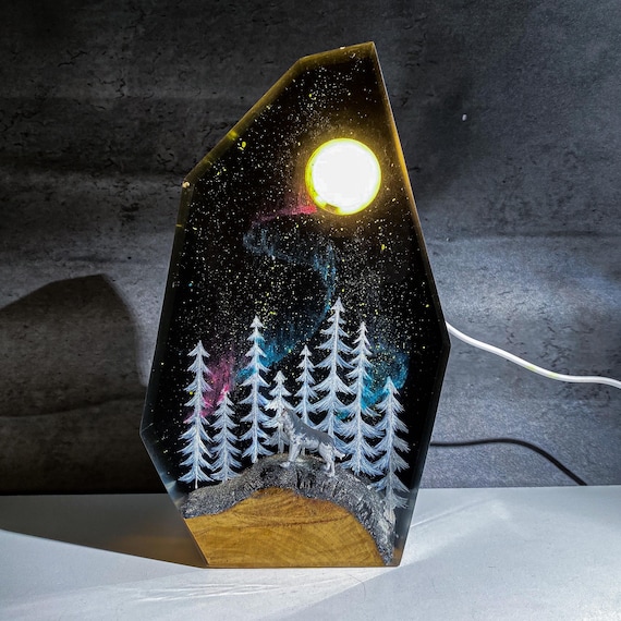 A howling wolf and pine tree scene hand-cast in glowing epoxy resin with a live-edge wood base — cabin-core art that actually lights up your room.