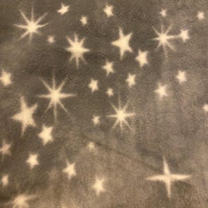 May include: A gray fleece blanket with a white star pattern. The stars are of different sizes and are scattered randomly across the blanket.