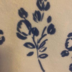 May include: A white fabric with a blue floral pattern. The flowers are stylized and resemble roses. The fabric has a soft, fuzzy texture.