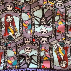 Puede incluir: Una tela colorida con un patr&oacute;n repetitivo de ventanas de vidrieras con Jack Skellington y Sally de Pesadilla antes de Navidad. Las ventanas est&aacute;n delineadas en negro y tienen un fondo morado.
