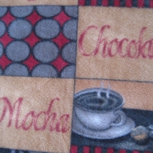 May include: A tan fabric with a patchwork design featuring a cup of coffee, the words "Mocha" and "Chocolate", and a pattern of red and gray circles.