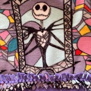 Puede incluir: Una manta de forro polar morada con un dise&ntilde;o de vidriera de colores que presenta a Jack Skellington de Pesadilla antes de Navidad. La manta tiene un borde de flecos morados.