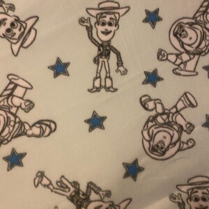 May include: A light blue fabric with a repeating pattern of black and white cartoon characters from the Toy Story movie. The characters include Woody, Buzz Lightyear, and a few stars.