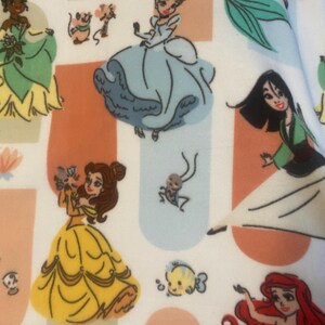 May include: A white fabric with a repeating pattern of Disney princesses. The princesses include Cinderella, Ariel, Belle, Tiana, and Mulan. Each princess is depicted in a different color dress and pose. The fabric is perfect for crafting projects, such as making clothing, bags, or home decor.