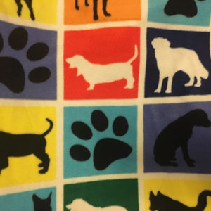May include: A colorful fabric featuring a repeating pattern of dog silhouettes and paw prints within square blocks. The squares are in various colors, including blue, red, yellow, and green, creating a playful and vibrant design.