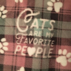 May include: A pink and green plaid fleece blanket with white paw prints and the text "Cats are my favorite people" with a heart in place of the "o" in people.