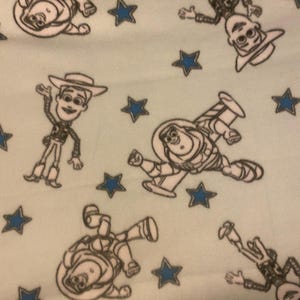 May include: A light blue fabric with a repeating pattern of white outlines of characters from the Toy Story movie. The characters include Woody, Buzz Lightyear, and the alien. The background is dotted with blue stars.